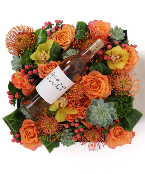 Desert Radiance BloomBox featuring orange and yellow roses, orchids, pincushion proteas, succulents, and greenery in a wooden crate