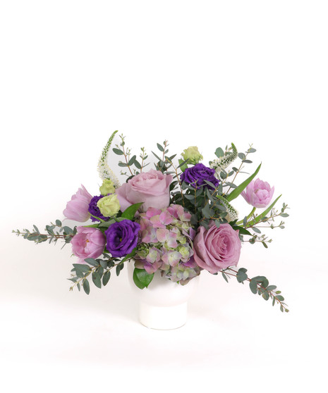 Amethyst Dream floral arrangement with lavender roses, purple lisianthus, pastel hydrangeas, and pink tulips in a white ceramic vase