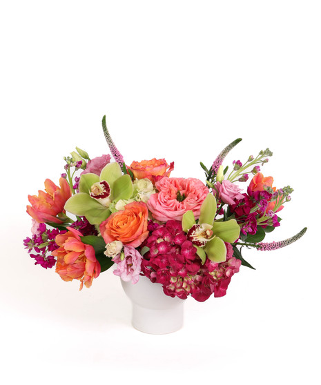 Flamingo Glow floral arrangement with coral garden roses, tulips, orchids, and hydrangeas in a white ceramic vase