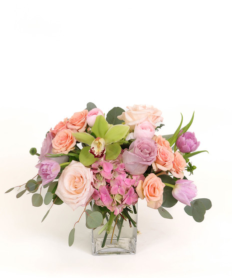 Ethereal Garden floral arrangement with blush and lavender roses, pink tulips, peach spray roses, and green orchids in a clear glass vase