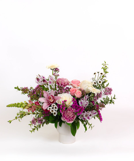 Mauve Melody floral arrangement with mauve roses, orchids, white gerbera daisies, and chamomile in a white ceramic vase