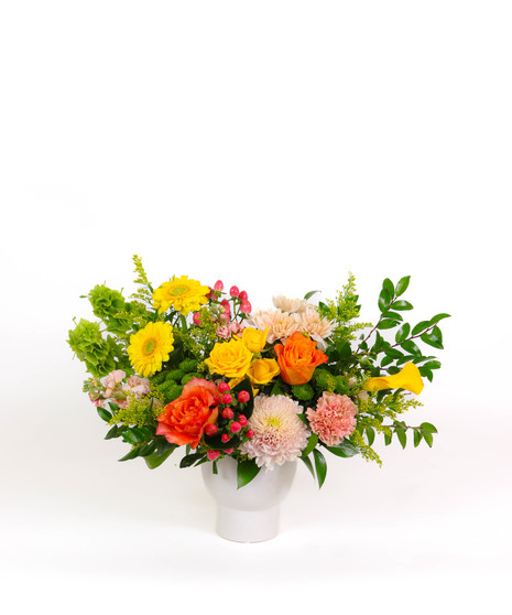 Sunshine & Sage floral arrangement with yellow roses, calla lilies, gerbera daisies, and bells of Ireland in a white ceramic vase