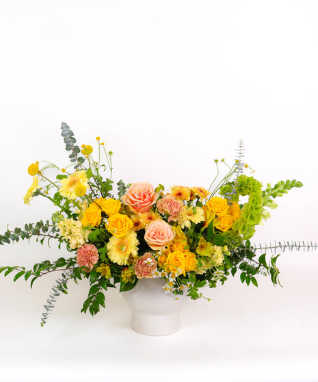 Sunset Cliffs floral arrangement with yellow and peach roses, craspedia, and golden mums in a white ceramic vase